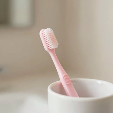 Warm editorial photography of a minimalist pastel pink toothbrush on a clean white ceramic holder, soft natural light, shallow depth of field, 35mm