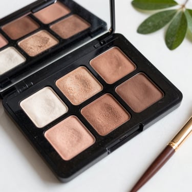 Extreme close-up of a high-contrast pressed eyeshadow palette, showing deep violet and metallic gold pans with velvet texture, low-key lighting.