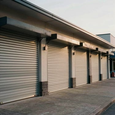A row of newly built retail shops with rolling shutters on a paved commercial street, natural lighting