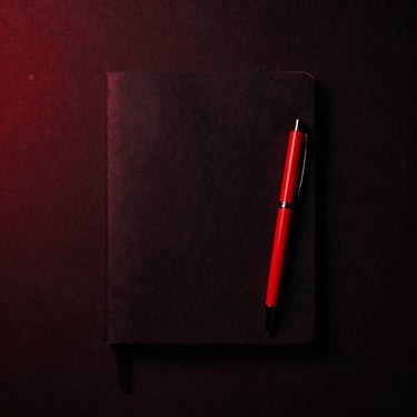 Overhead flatlay of minimalist workspace with a black notebook and red pen, high contrast studio photography, dramatic red and black lighting, 50mm