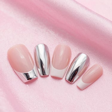 Macro photograph of perfectly sculpted prosthetic nails with modern silver metallic details, held against a soft powder pink silk background, bright high-key lighting