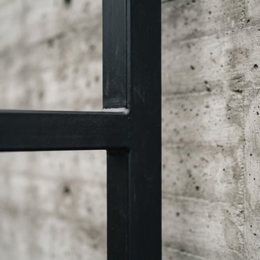 Macro architectural photography of a clean minimalist matte black metal gate joint, overcast daylight, desaturated industrial tones, showing perfect seamless weld