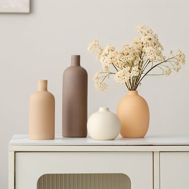 Collection of minimalist ceramic vases in earth tones and white with dried flowers on a modern sideboard.