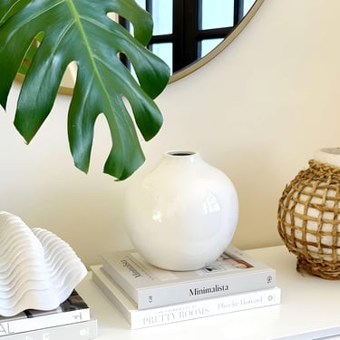 White ceramic vase on minimalist coffee table books with a monstera leaf and coastal decor.