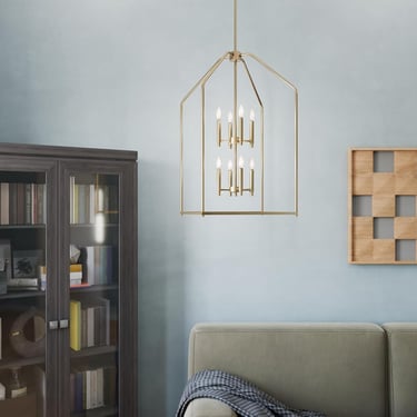 Modern gold lantern chandelier hanging in a living room with a grey bookcase and sage sofa.