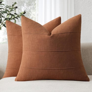 Pair of burnt orange textured decorative throw pillows with horizontal stitching on a neutral sofa.