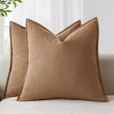 Pair of brown linen decorative throw pillows with flanged edges on a light-colored sofa.