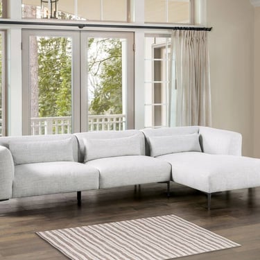 Modern light gray sectional sofa with chaise lounge on dark wood floors in a bright living room.