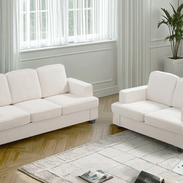 Modern white fabric sofa set and matching loveseat on a textured rug in a bright living room.
