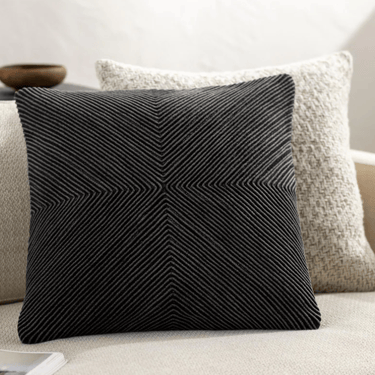Modern black decorative throw pillow with a geometric ribbed texture on a white sofa.