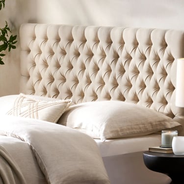 Cream tufted headboard with linen bedding and decorative pillows in a modern bedroom.