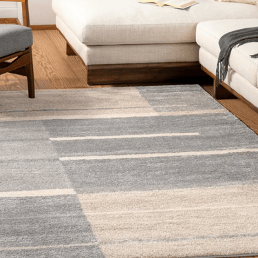 Modern gray and cream geometric area rug under a white sectional sofa in a bright living room.