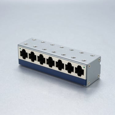 Industrial DIN-rail network switch, solid clinical light-gray metallic background, cold studio lighting.