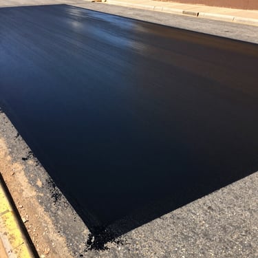 Freshly applied black liquid road sealer on an asphalt driveway, showing a clean matte black finish under bright sun
