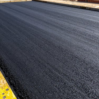 Close-up of freshly laid, steaming hot-mix asphalt showing rich black aggregate texture under bright high-contrast daylight
