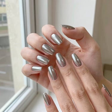 Detailed view of metallic chrome nail art on almond-shaped extensions, bright editorial photography, soft natural window light, warm neutral tones, crisp focus.