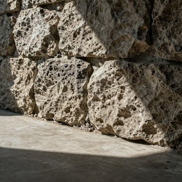 Extreme close-up of rough-hewn stone wall meeting a smooth concrete floor, dramatic shadow line, natural textures.