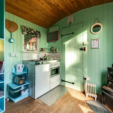 Cozy cabin interior with a compact kitchenette, mint green wood walls, and a vintage wood-burning stove.