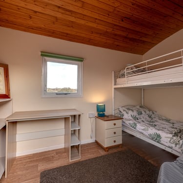 Bedroom with bunk beds, a study desk, and wood paneling on the ceiling.