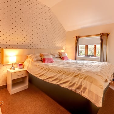 Cozy modern bedroom with a striped duvet, warm lamp lighting, and patterned wallpaper.