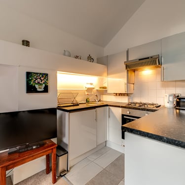 Modern studio apartment kitchen with white cabinets, dark countertops, and integrated appliances.