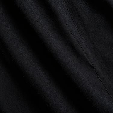 Low-key close-up of heavy black cotton fabric texture, showing the coarse weave and structural seams under dramatic side-lighting, high contrast, 35mm film