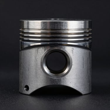 Isolated high-contrast shot of a forged steel engine piston, dark background, side-lit