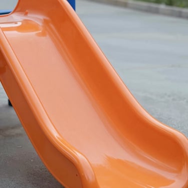 Heavy-duty rotational-molded PE slide component, smooth orange plastic surface, clean engineering focus.
