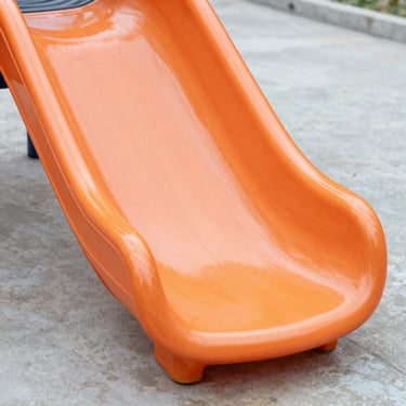 Close-up of a vibrant orange rotational-molded PE slide, smooth thick plastic texture, outdoor daylight