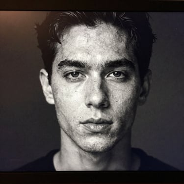 A digital screen showing a high-contrast black and white portrait with organic film grain, soft warm tones in the midtones