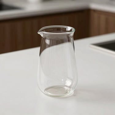 A minimalist double-walled glass coffee brewer sitting on a clean white countertop.