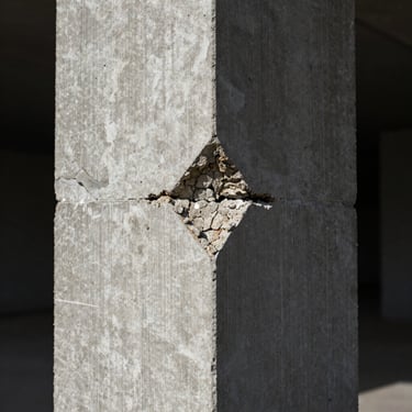 Macro shot of concrete micro-fractures and severe corrosion on a structural pillar, illuminated by stark directional lighting in a dark environment.