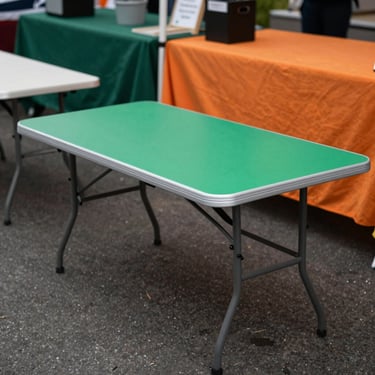 Portable folding table with a durable surface, set up at a market stall, ready for product display, overcast daylight.