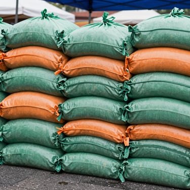 Heavy-duty sandbags or water weights securing the legs of a market tent, close-up shot showing stability, overcast daylight.