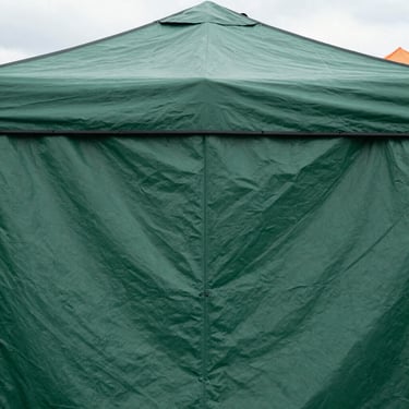 Close-up of a sturdy, waterproof market tent fabric in forest green, overcast daylight, showing texture and durability.