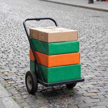 Portable hand truck or trolley for transporting market supplies, loaded with boxes, on a cobblestone street, overcast daylight.