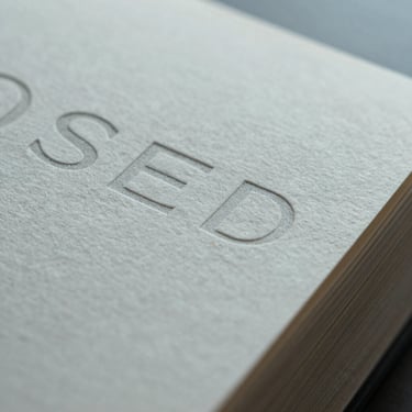 Extreme close-up macro crop of premium textured paper packaging with subtle embossed typography under cool overcast light.