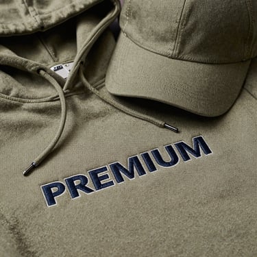 Premium brand merchandise including a heavy-cotton hoodie and structured cap, showcasing flawless embroidery details and thick fabric weight.