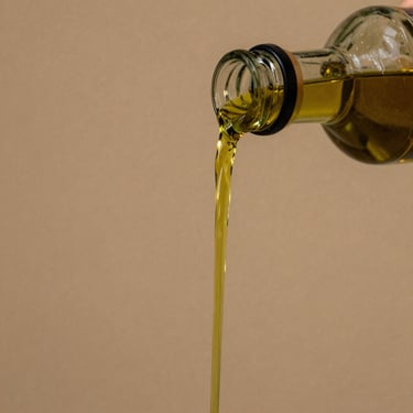 Tight macro shot of rich golden-green olive oil being poured from an estate bottle, warm editorial photography, rich earthy tones