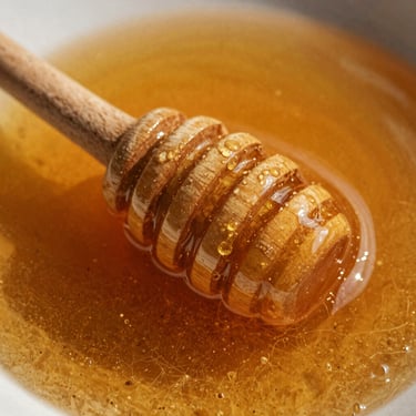 Tight macro shot of thick raw wild honey on a wooden dipper, warm editorial photography, high-contrast Mediterranean sunlight