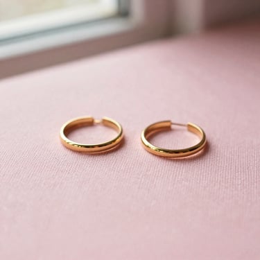 Delicate gold earrings and rings on a soft pink linen surface, macro shot, warm lighting