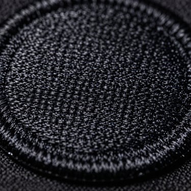 Extreme close-up of a high-density embroidered patch, showing tight thread weave and thick merrowed border, hard side-lighting