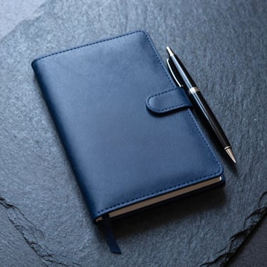 Tight detail of a minimalist leather notebook and sleek fountain pen on a dark slate desk, cool daylight