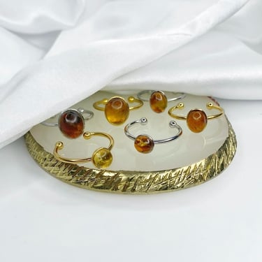Anillos con piedras Ámbar sobre una superficie de exhibición y una tela de seda medio recubriéndolos. 