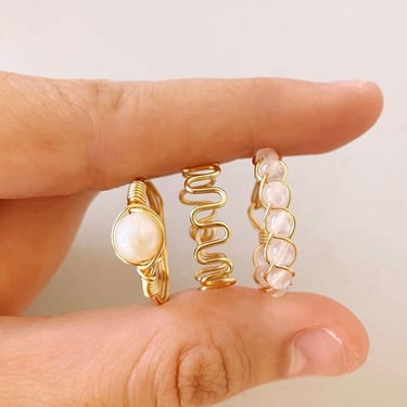 Anillos dorados con cuentas color crema claro agarrados por dos dedos.