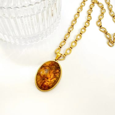 Cadena dorada con una piedra grande de Ámbar sobre una superficie blanca. 