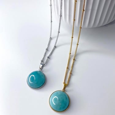 Cadenas dorada y plateada con piedra grande de Larimar sobre una superficie blanca.