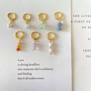 Aretes dorados con diferentes tipos de cuentas de colores sobre una pagina de un libro.