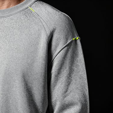 Close-up of engineered shoulder seams on a heavy-weight gray sweatshirt, high-contrast studio light highlighting the dense knit structure.