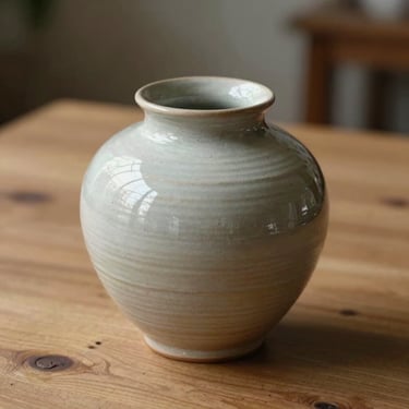 Intimate close-up of a handmade ceramic vessel on a raw oak table, soft side light.